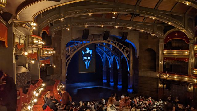 Interior of a theater with ornate ceiling, stage lighting, and audience seating visible.