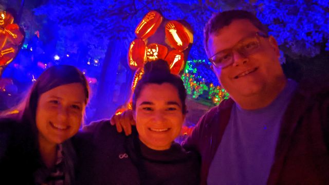 Three people at an event with colorful neon signage and blue lighting in the background.