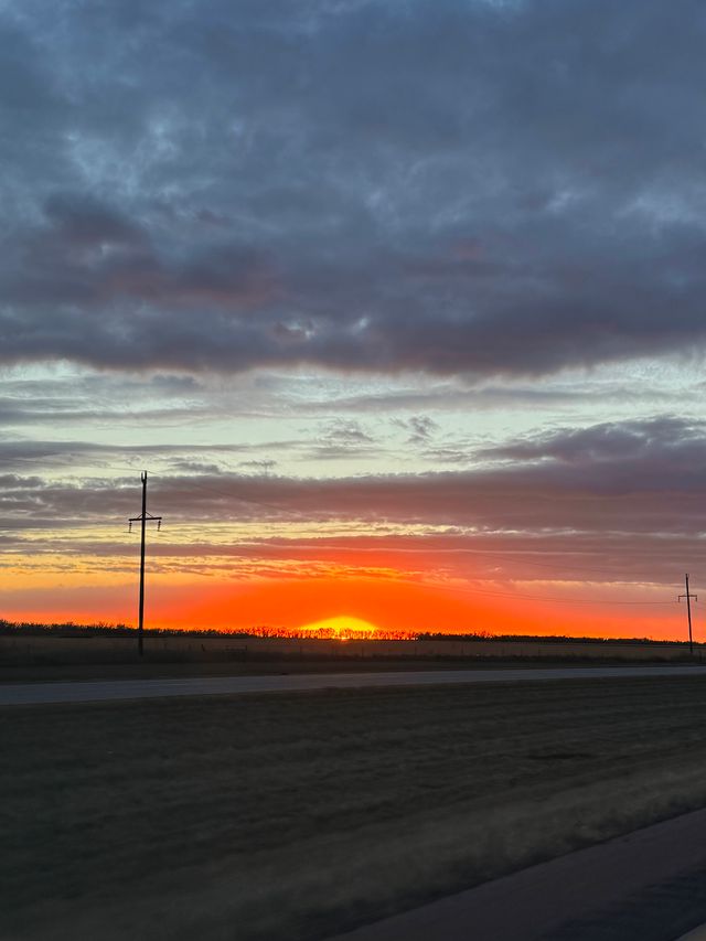 Vivid orange and red sunset over a flat highway landscape with utility poles.