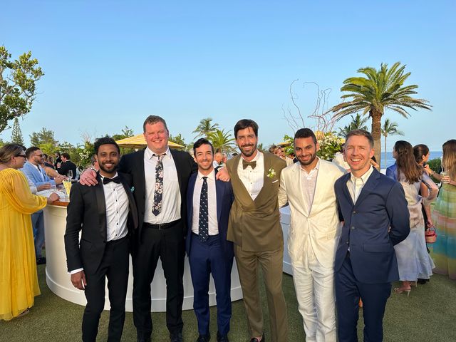 Six men in formal attire posing together at an outdoor wedding reception with palm trees.