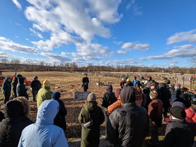 A crowd of people gathered outdoors at a wintry open field event under blue skies.