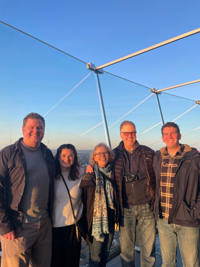 Five people posing together on an outdoor observation deck at sunset with a city skyline behind them.