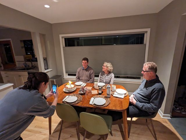 Four people seated around a dinner table in a warmly lit home dining room.