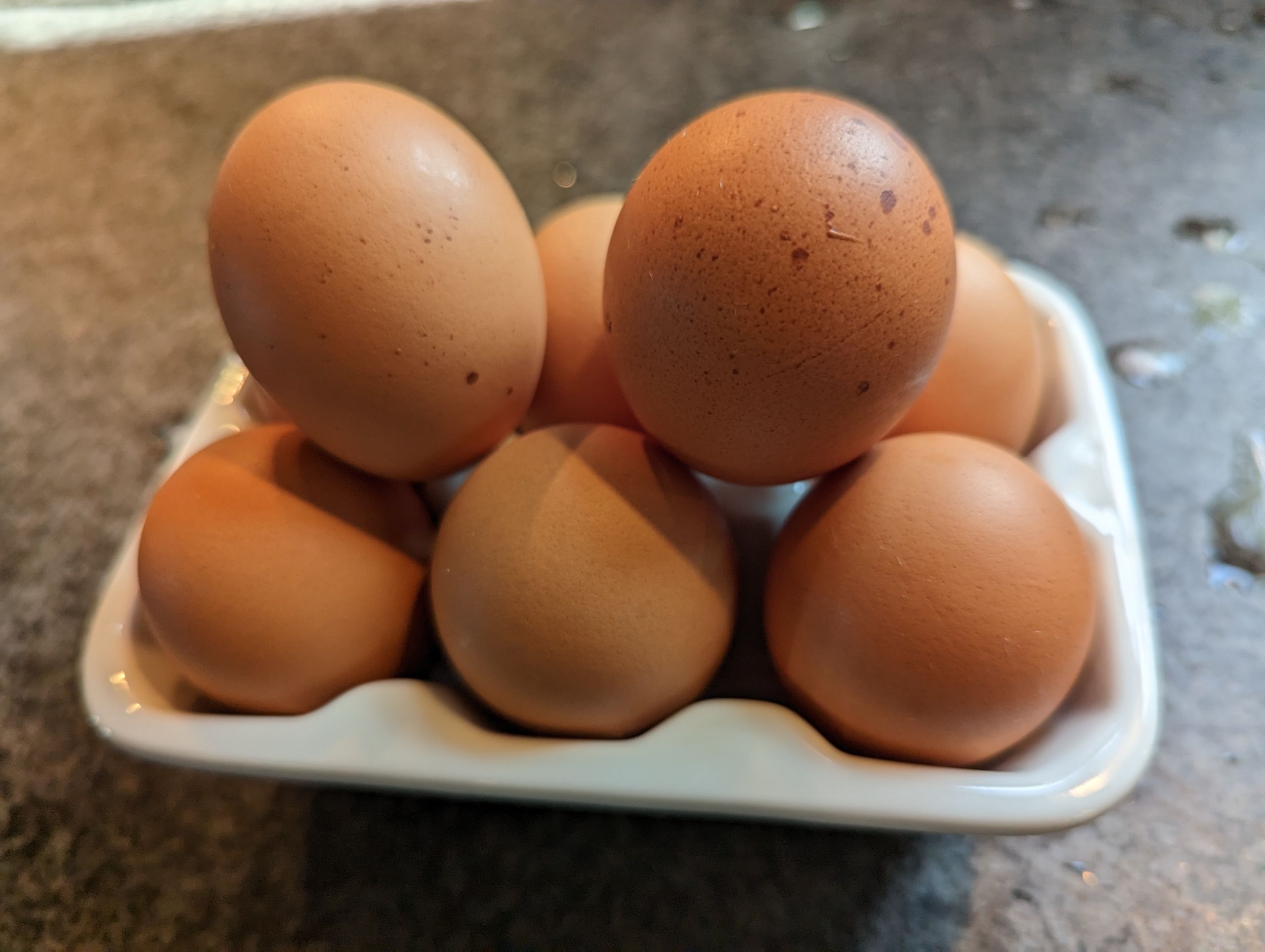Several brown eggs are piled in a white ceramic egg holder on a countertop.