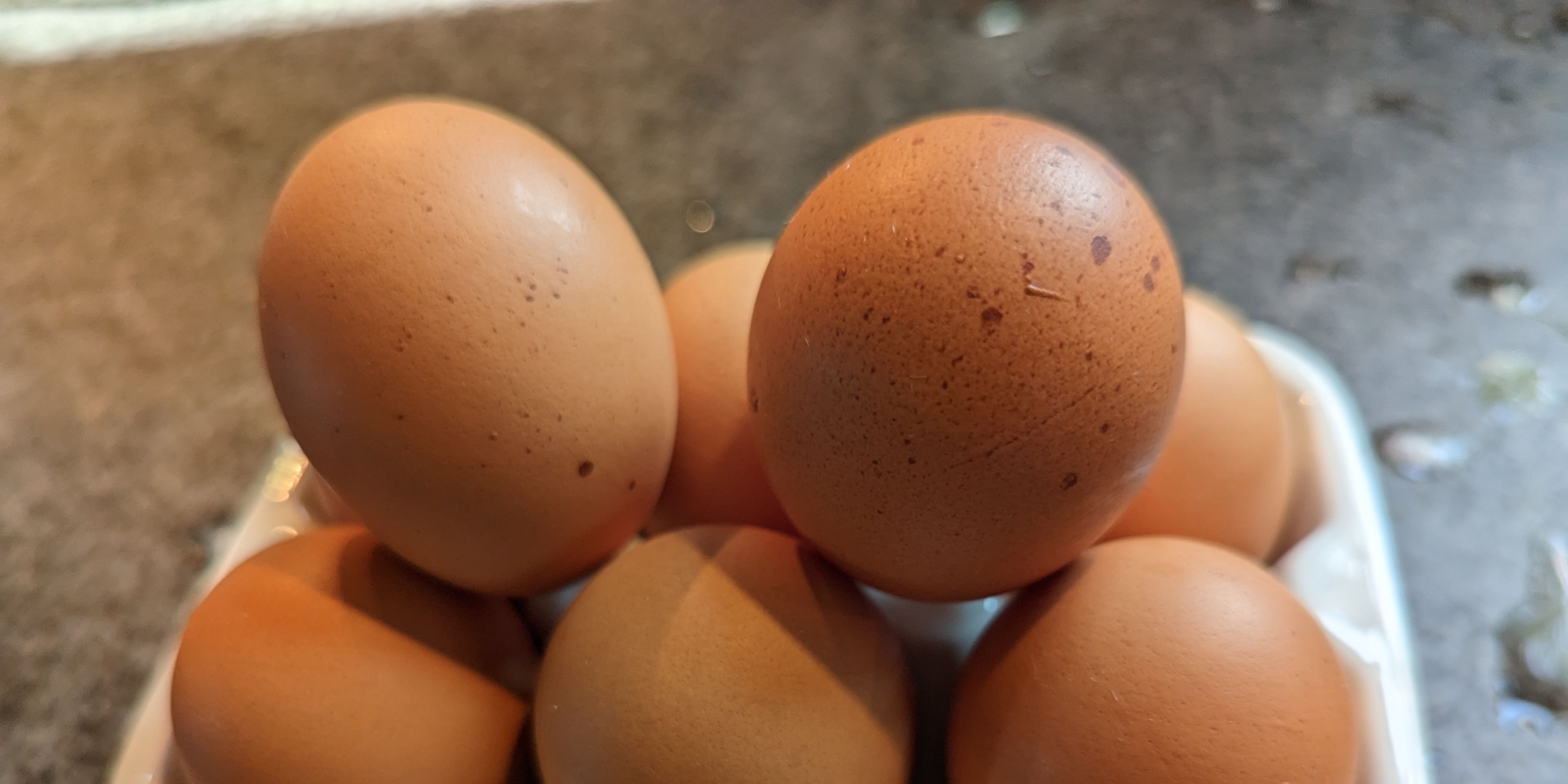 Several brown eggs are piled in a white ceramic egg holder on a countertop.